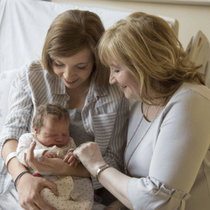 New mom and Grandmother laying on hospital bed and admiring a newborn child