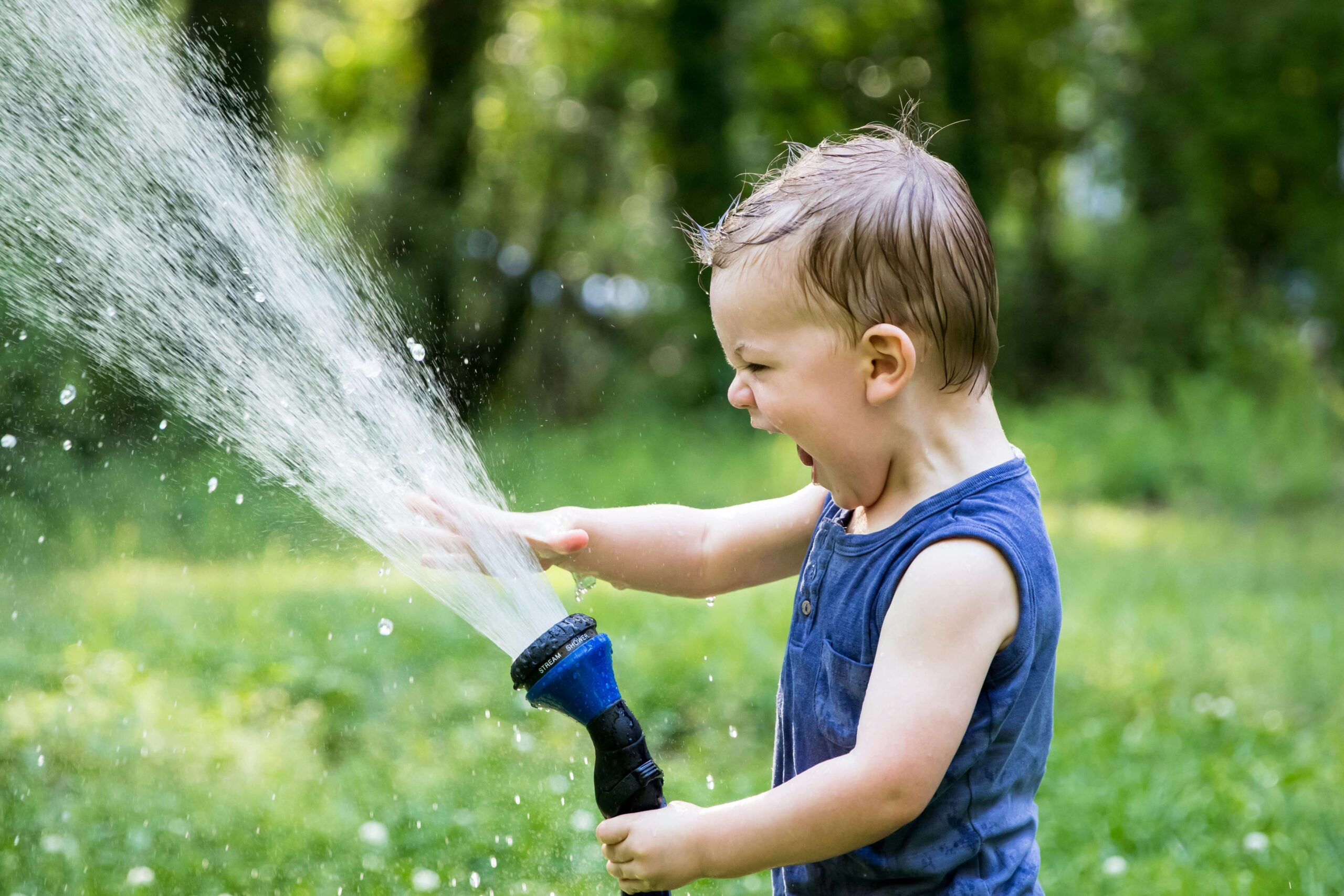 toddler playing with water coming out of hose