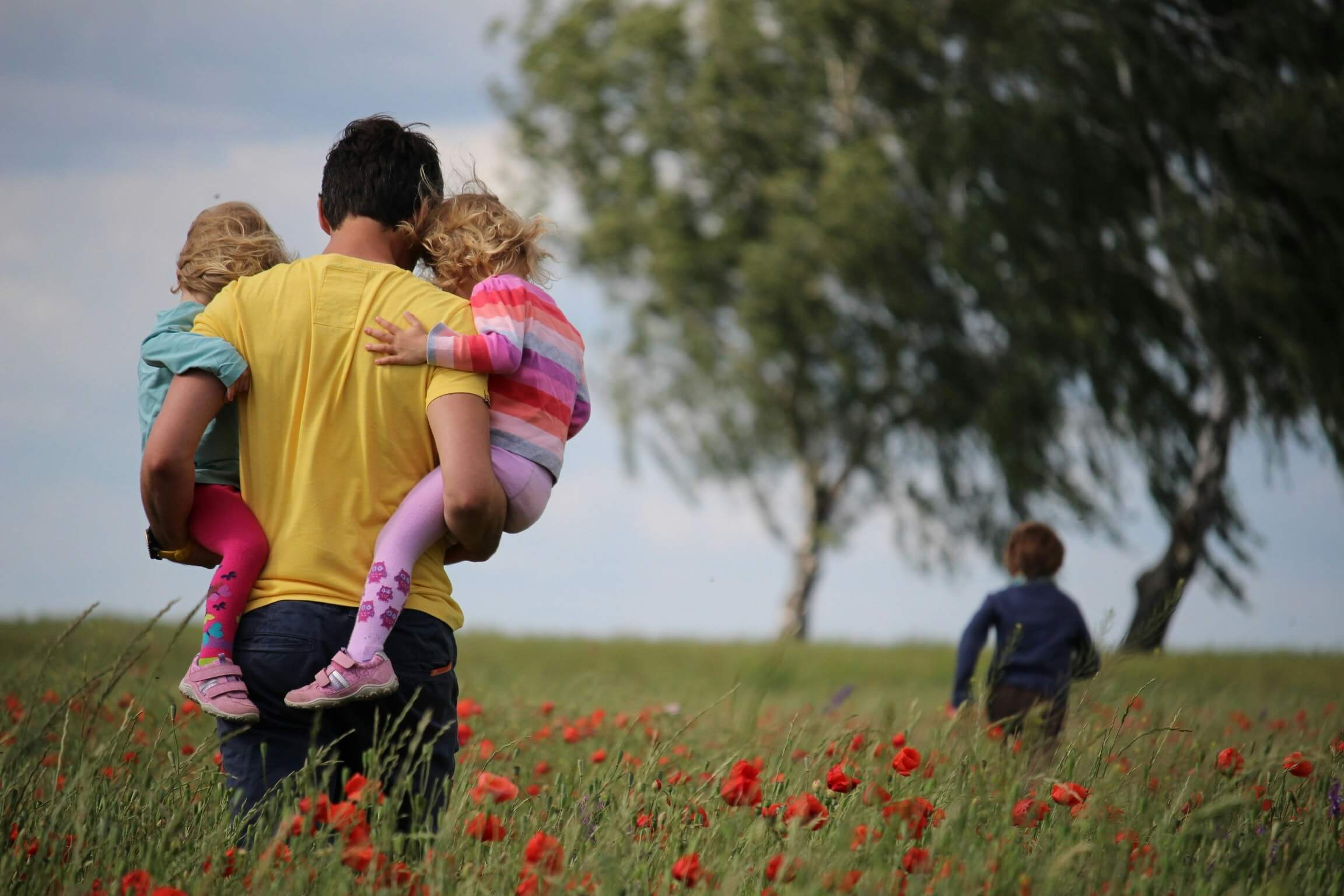 man holding two girls in a field of red flowers and boy running