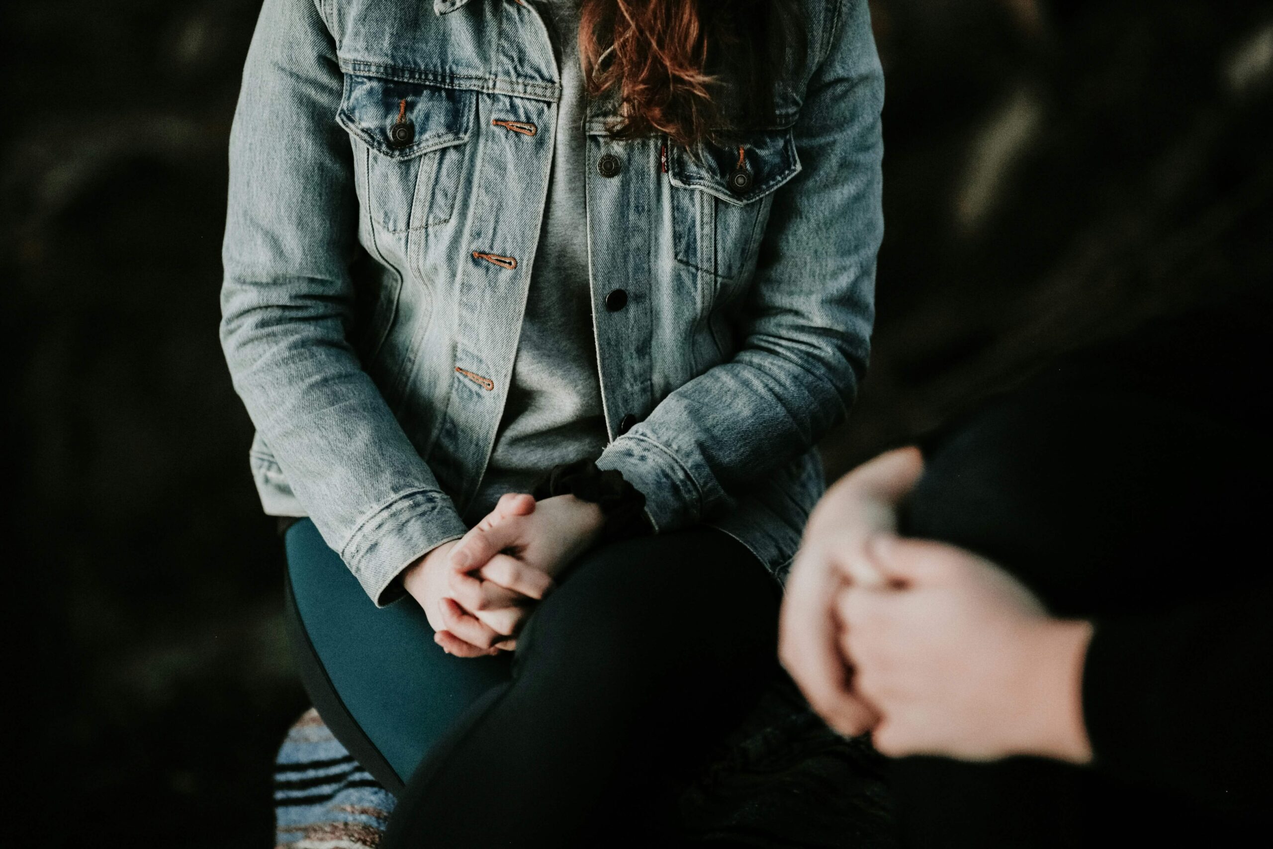 woman with jean jacket sitting with hands folded next to person sitting with hands folded