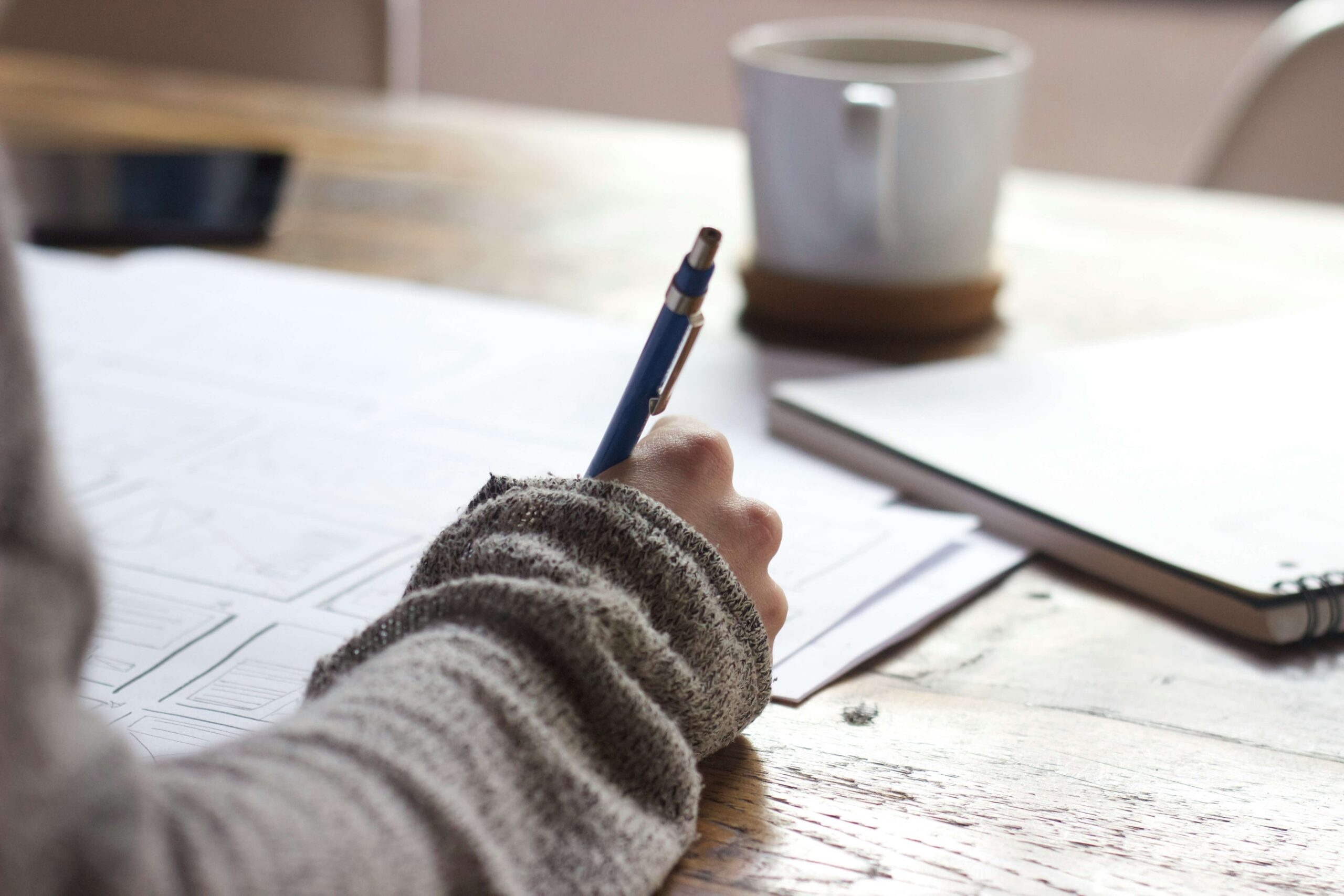 person holding pen writing on paper on desk