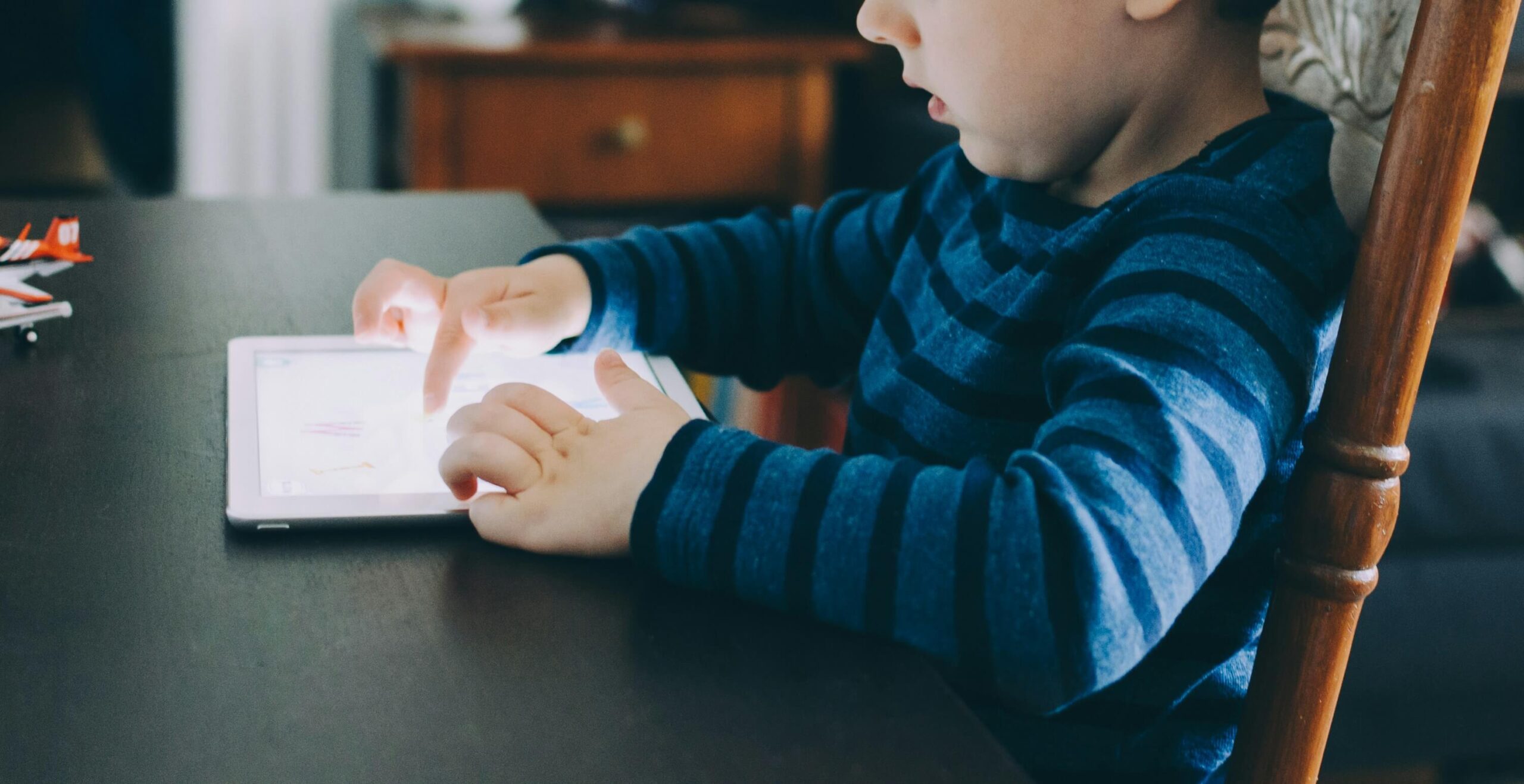 young child sitting at table playing on iPad