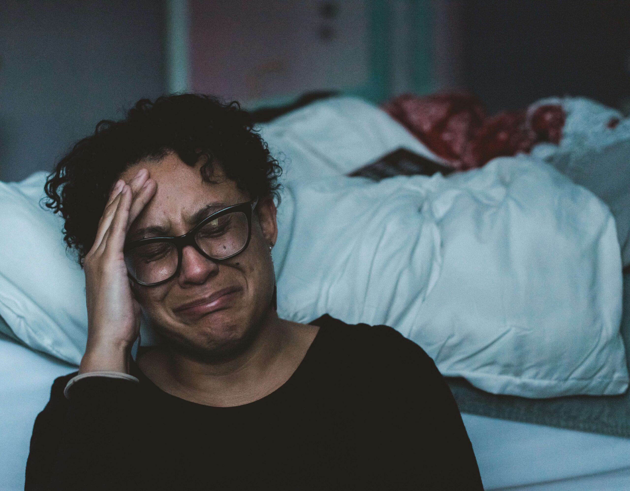 mom sitting at edge of bed crying with hand on head