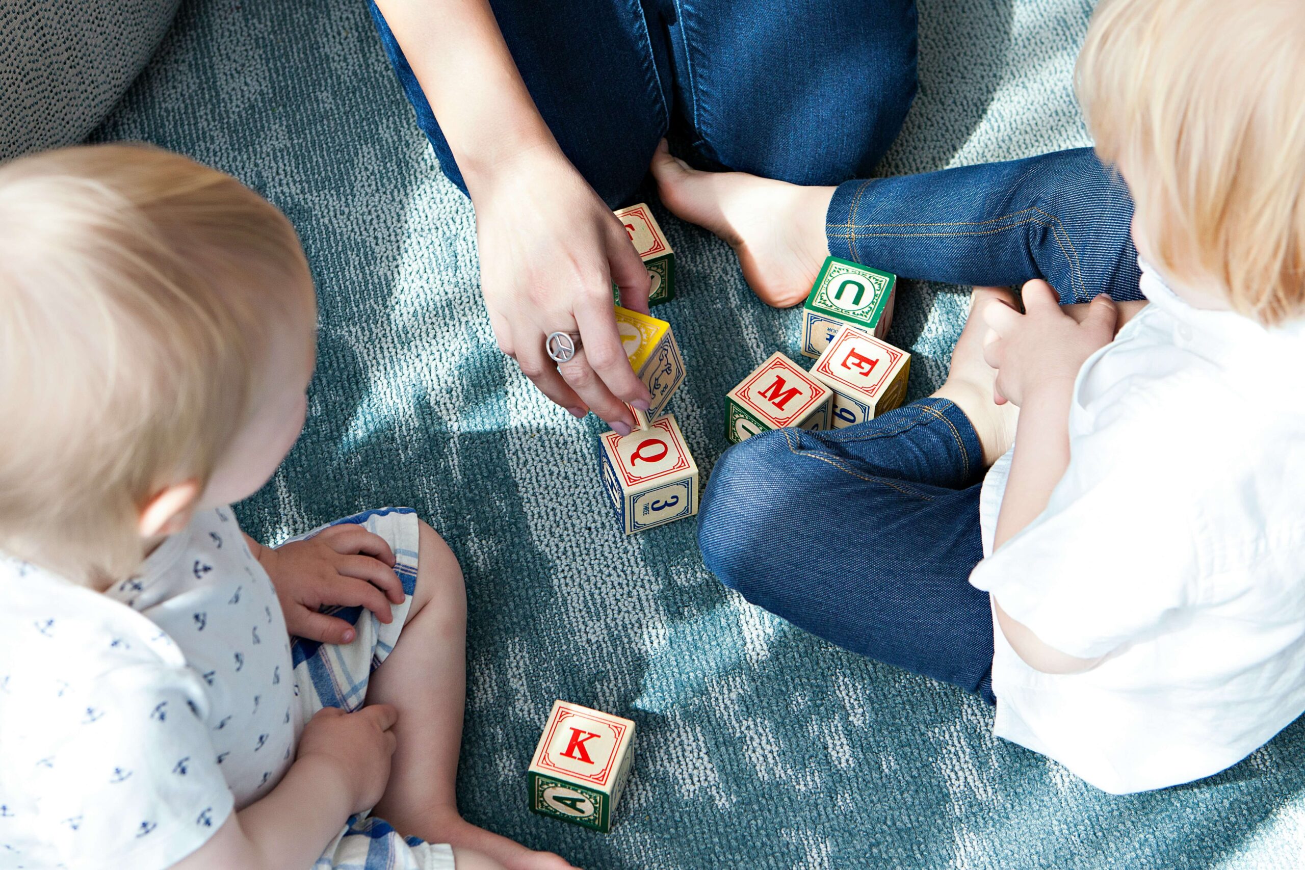 adult sitting on floor with two children playing with blocks