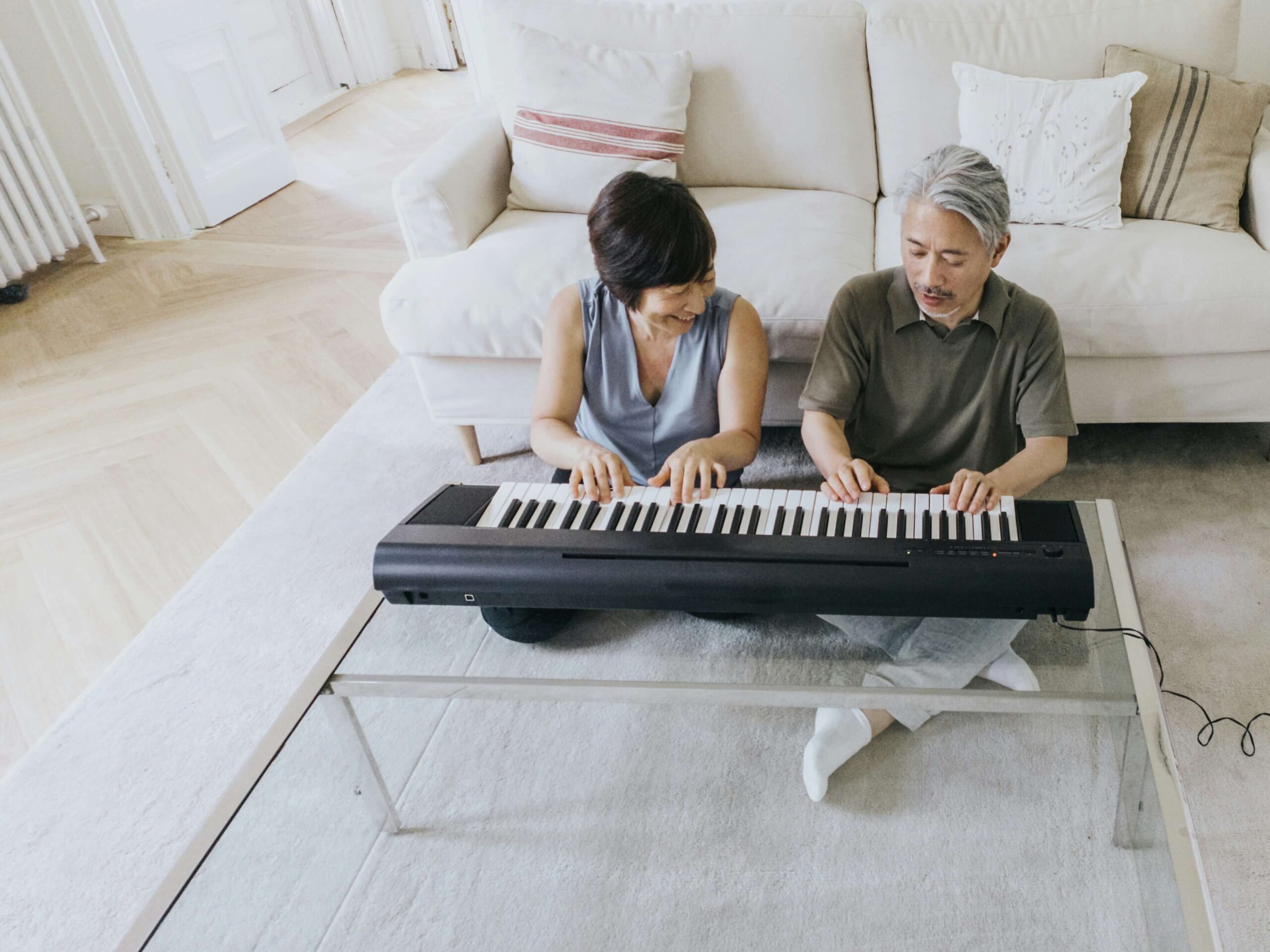 woman and man sitting on ground next to each other laughing and playing keyboard piano.