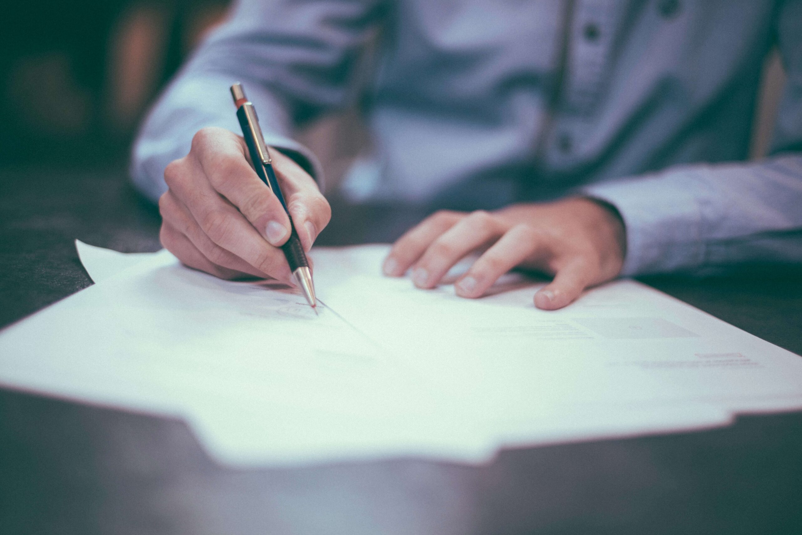 adult using pen to write on sheets of paper on desk