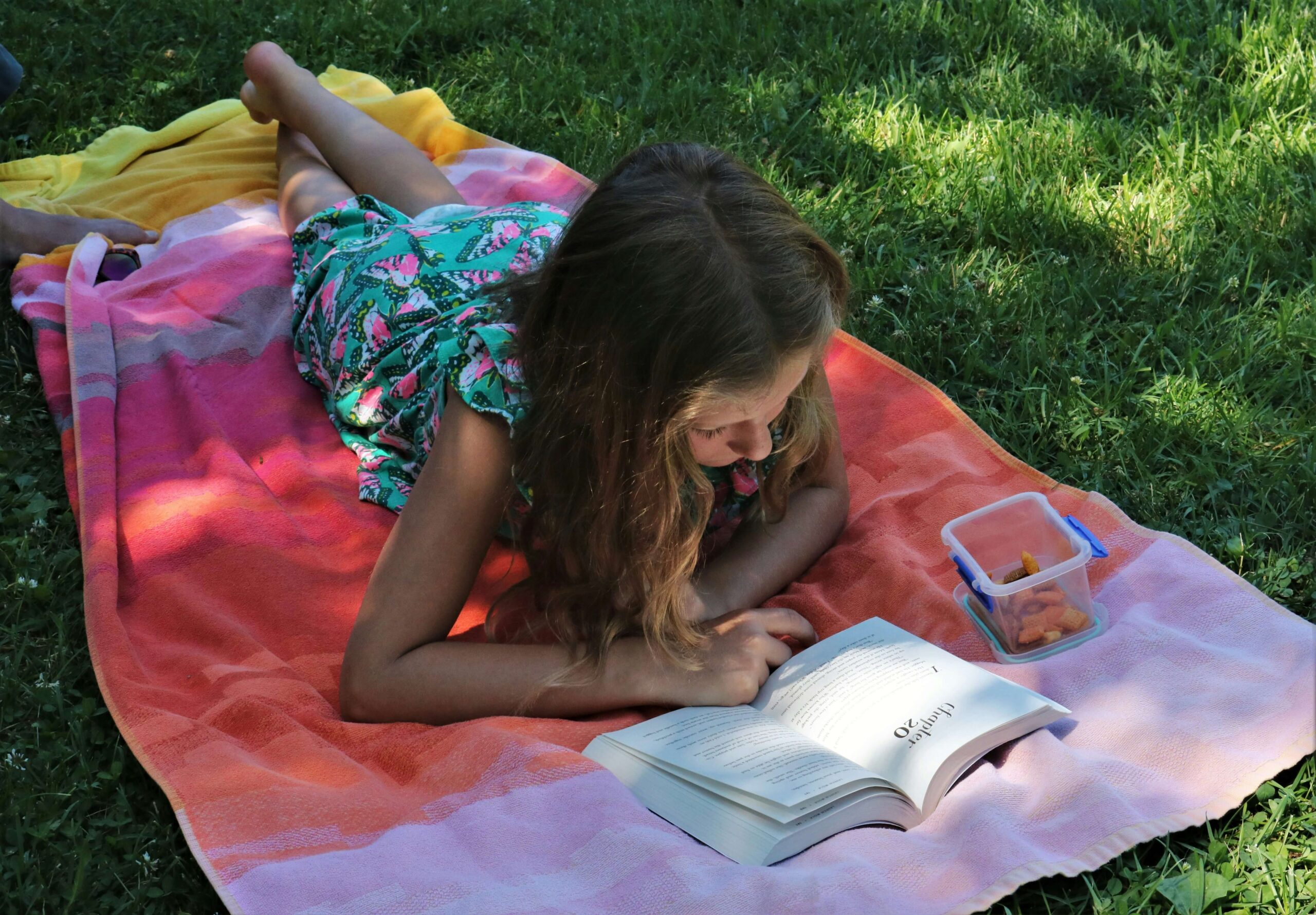 young girl laying on towel reading a book
