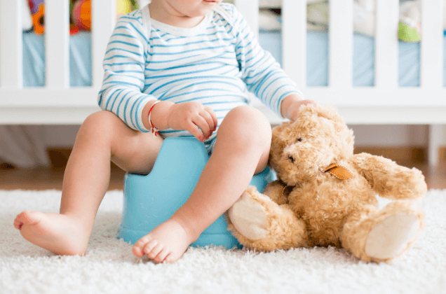 young child sitting in potty chair next to stuffed bear