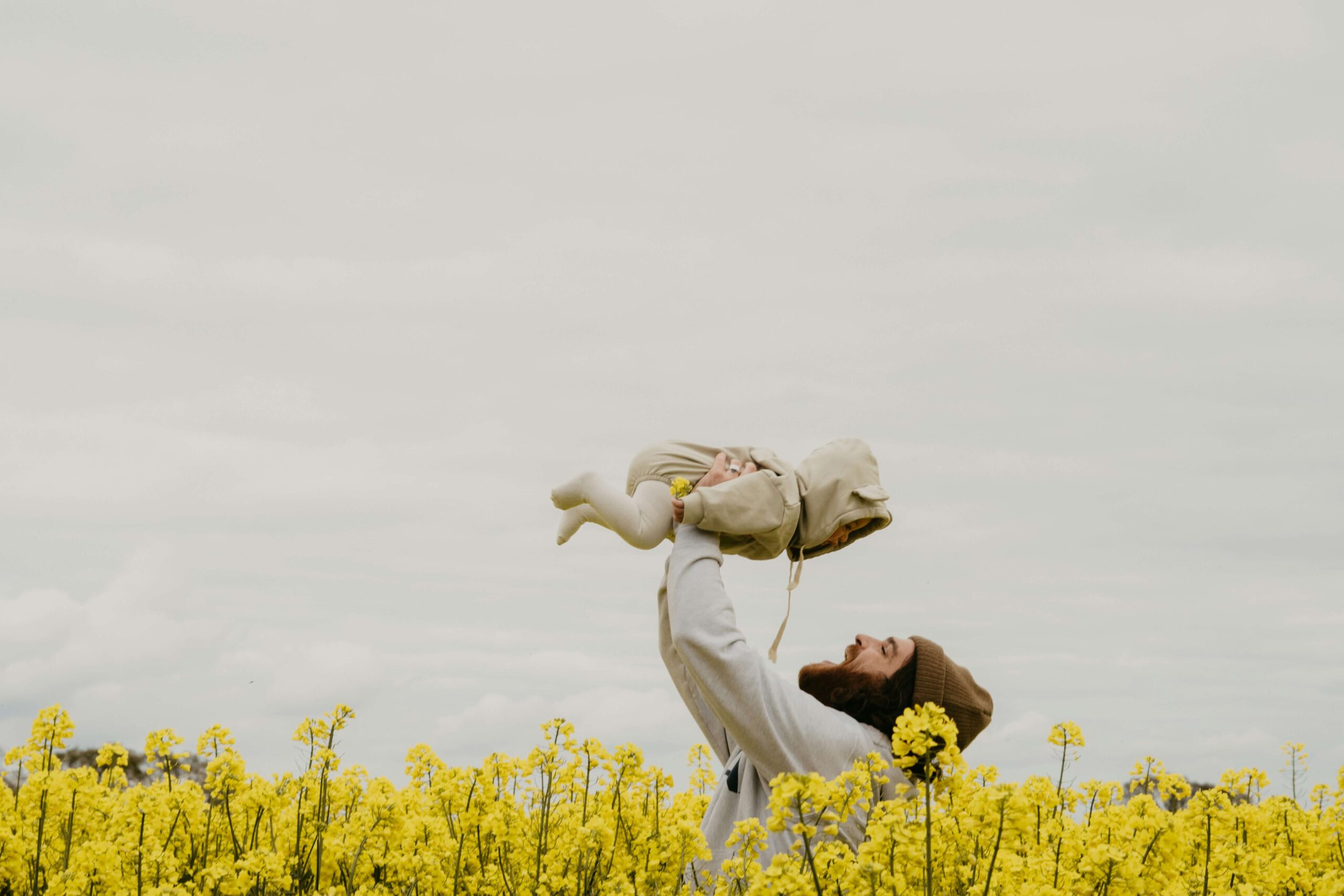 dad holding baby up in air smiling in a field of yellow flowers