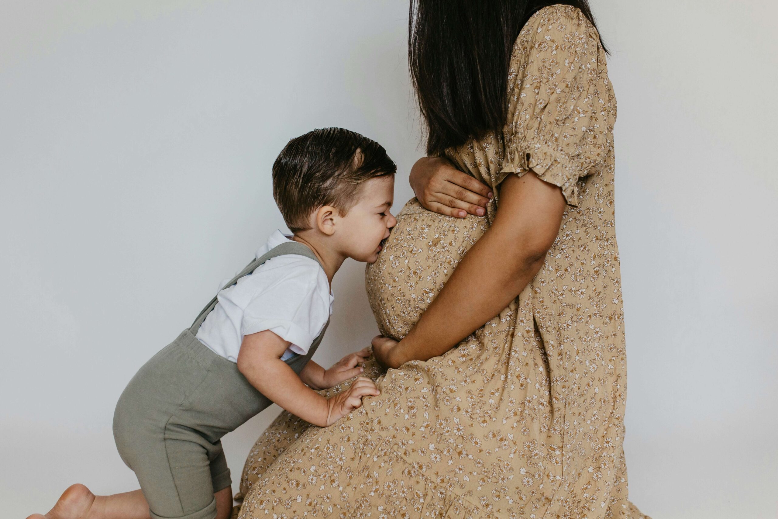 young boy kissing pregnant belly of mother