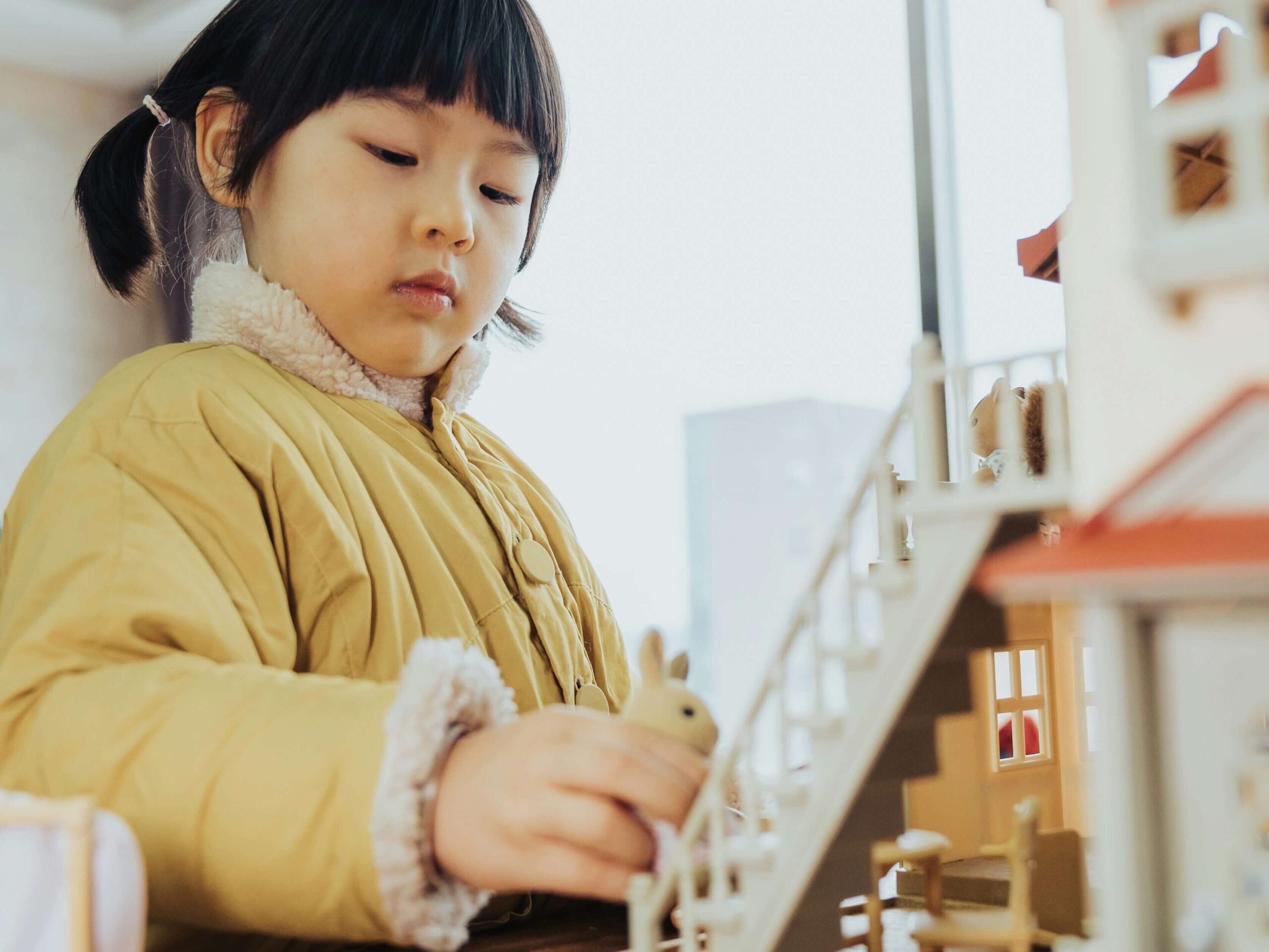 young girl playing independently with doll house