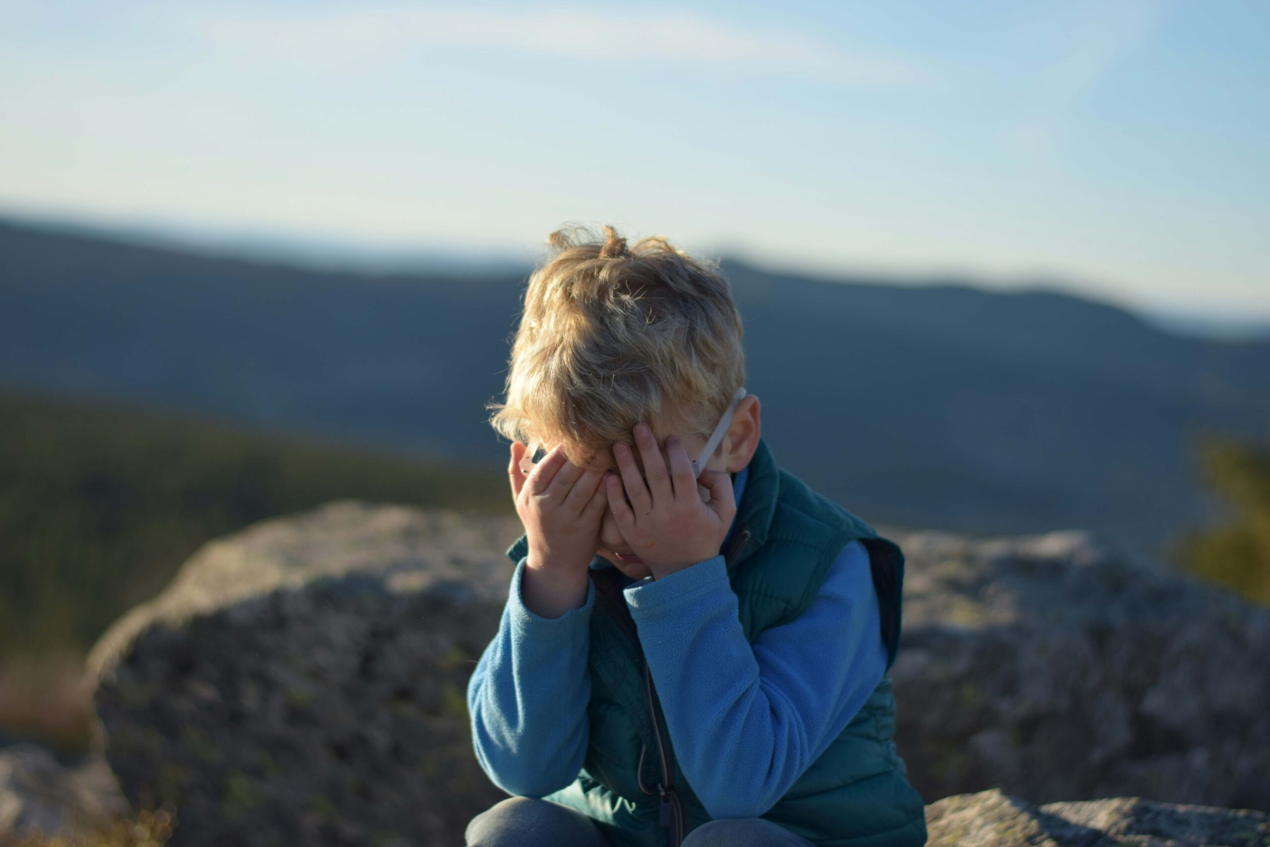 young boy sitting outside with hands covering face