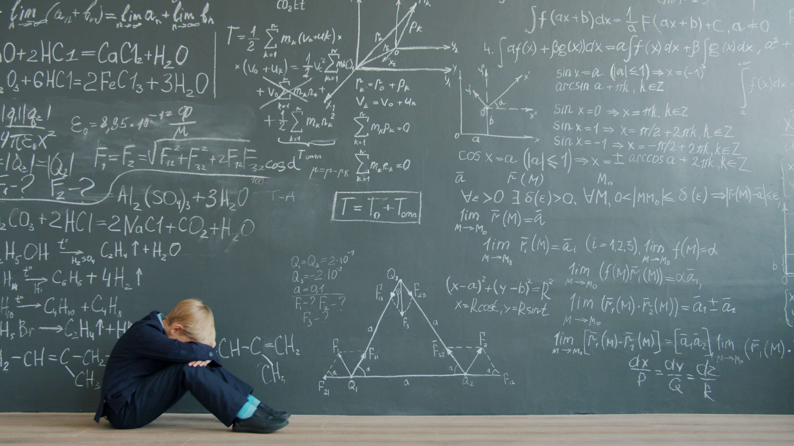 young boy sitting on floor with head in hands with chalkboard behind him